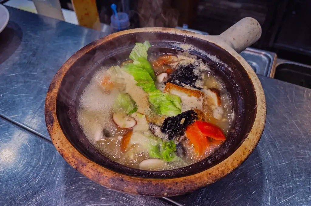 Steaming claypot balanced fish soup with pomfret fish, shiitake mushrooms, napa cabbage, seaweed and tomato in a naturally collagen-rich fish bone broth at Hup Lok, photographed from a high-angle overhead view.