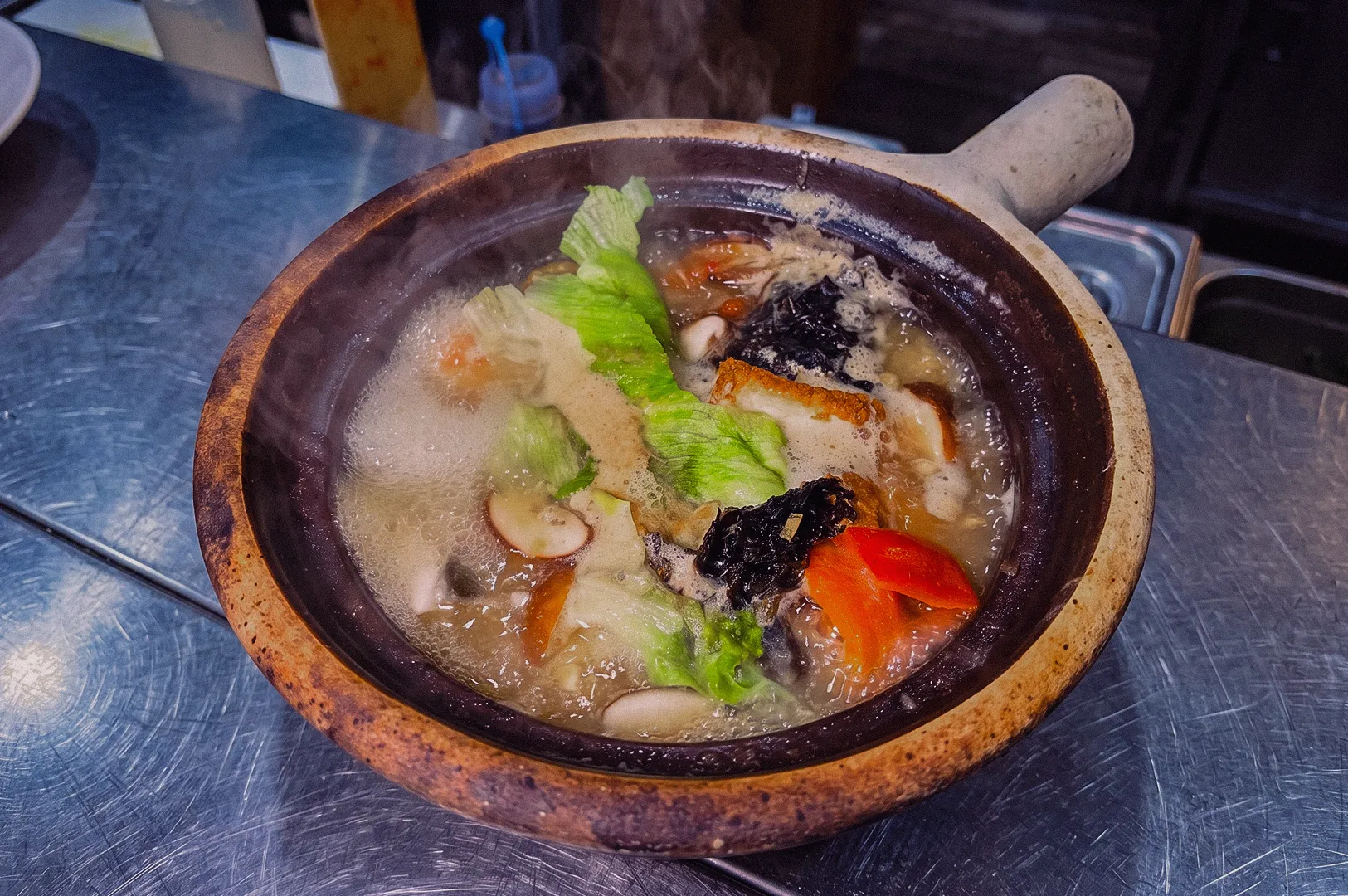 Steaming claypot balanced fish soup with pomfret fish, shiitake mushrooms, napa cabbage, seaweed and tomato in a naturally collagen-rich fish bone broth at Hup Lok, photographed from a high-angle overhead view.