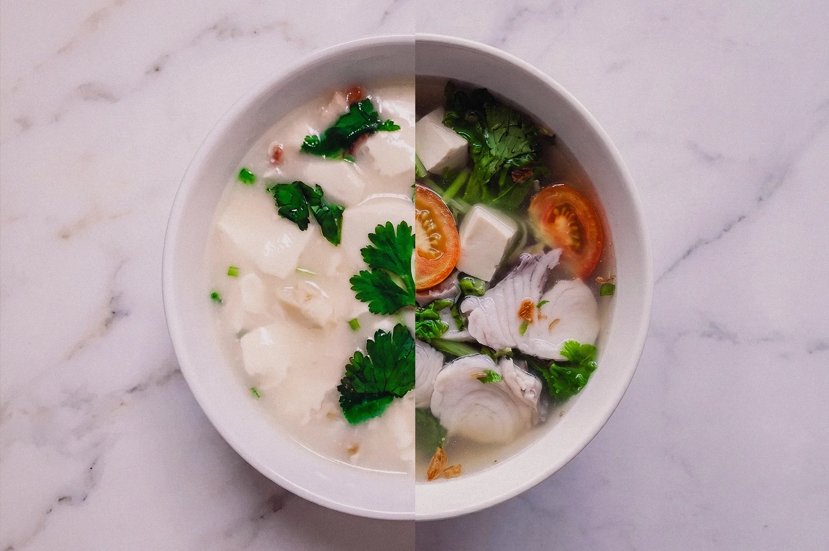 Top-down overhead shot of a white porcelain bowl split in half, comparing creamy milky fish soup with silken tofu and fresh coriander on the left side against clear Teochew-style fish soup featuring sliced fish fillets, tomatoes, tofu, and green vegetables on the right side over a light marble table.