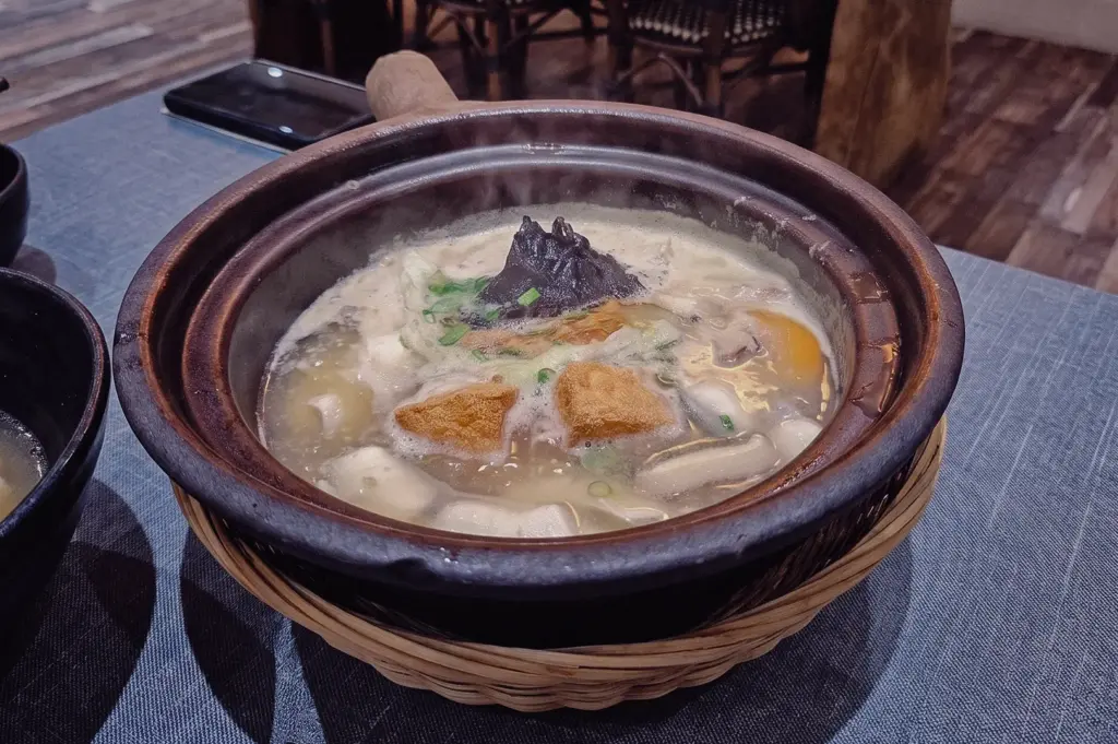 Three-quarter overhead shot of a claypot pomfret fish soup at a restaurant, featuring rich collagen broth, fish slices, tofu, seaweed, and vegetables, showcasing a generous fish soup portion size.