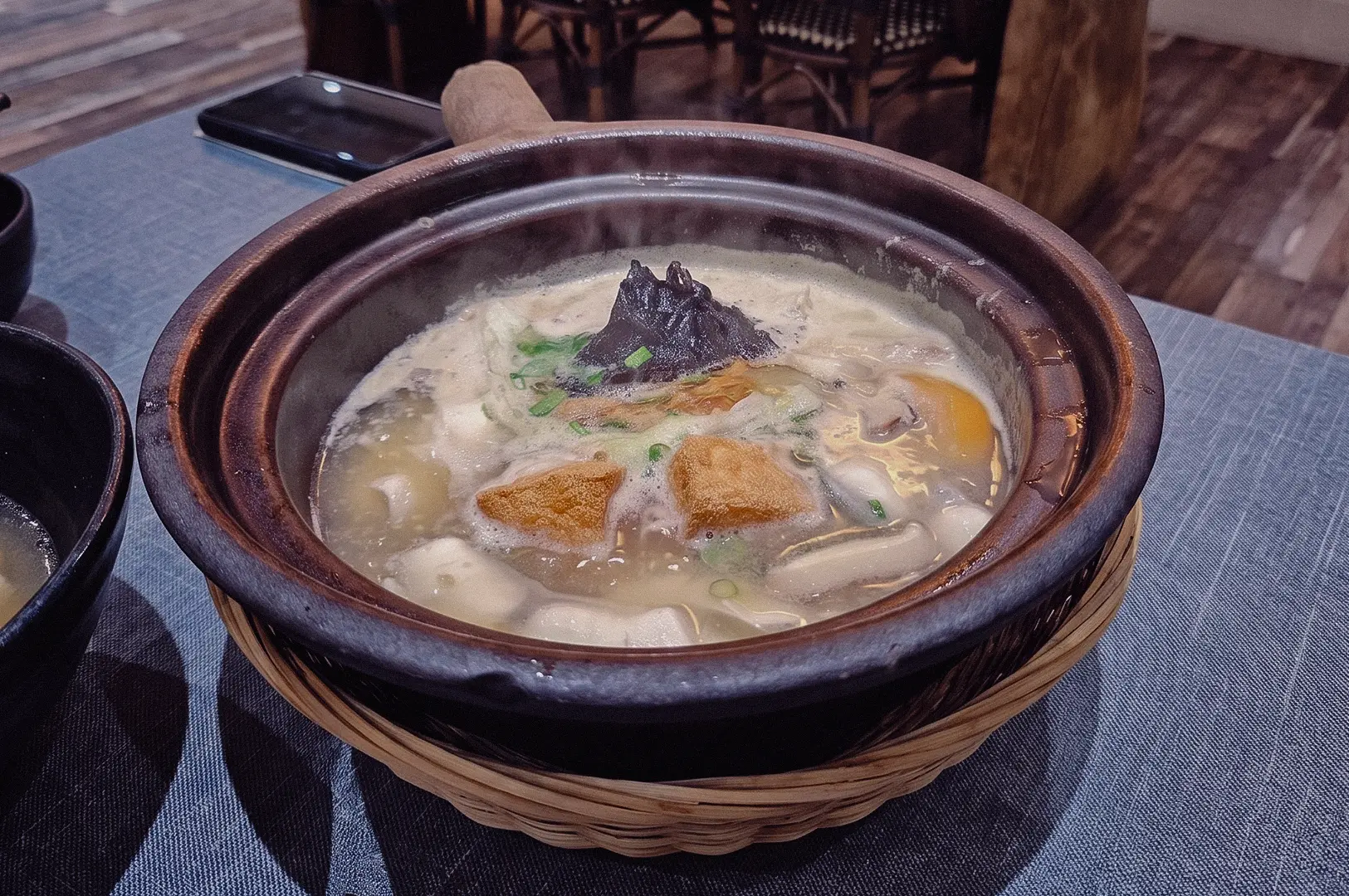 Three-quarter overhead shot of a claypot pomfret fish soup at a restaurant, featuring rich collagen broth, fish slices, tofu, seaweed, and vegetables, showcasing a generous fish soup portion size.