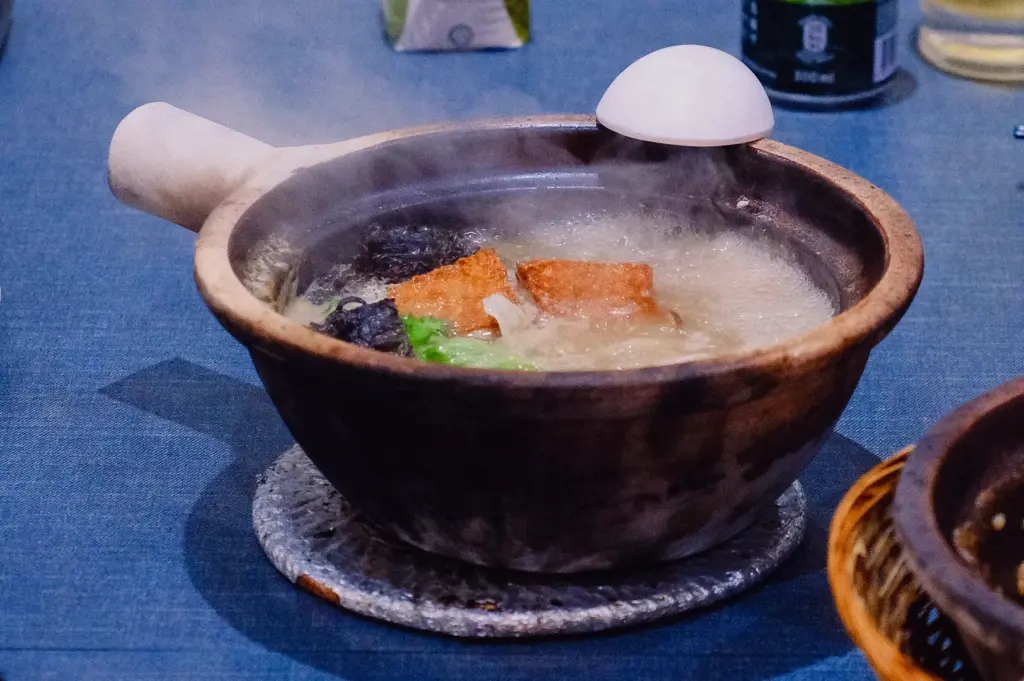 Steaming bowl of traditional fish soup in Singapore with collagen-rich fish broth, vegetables and fish slices served in a clay pot, captured in an eye-level close-up shot highlighting the thick, natural fish-based soup.
