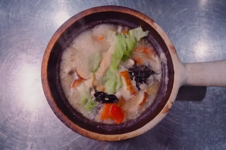 Overhead shot of steaming pomfret fish soup in a traditional claypot, featuring tender pomfret slices, cabbage, shiitake mushrooms, seaweed, and tomato in a rich collagen-based fish broth.