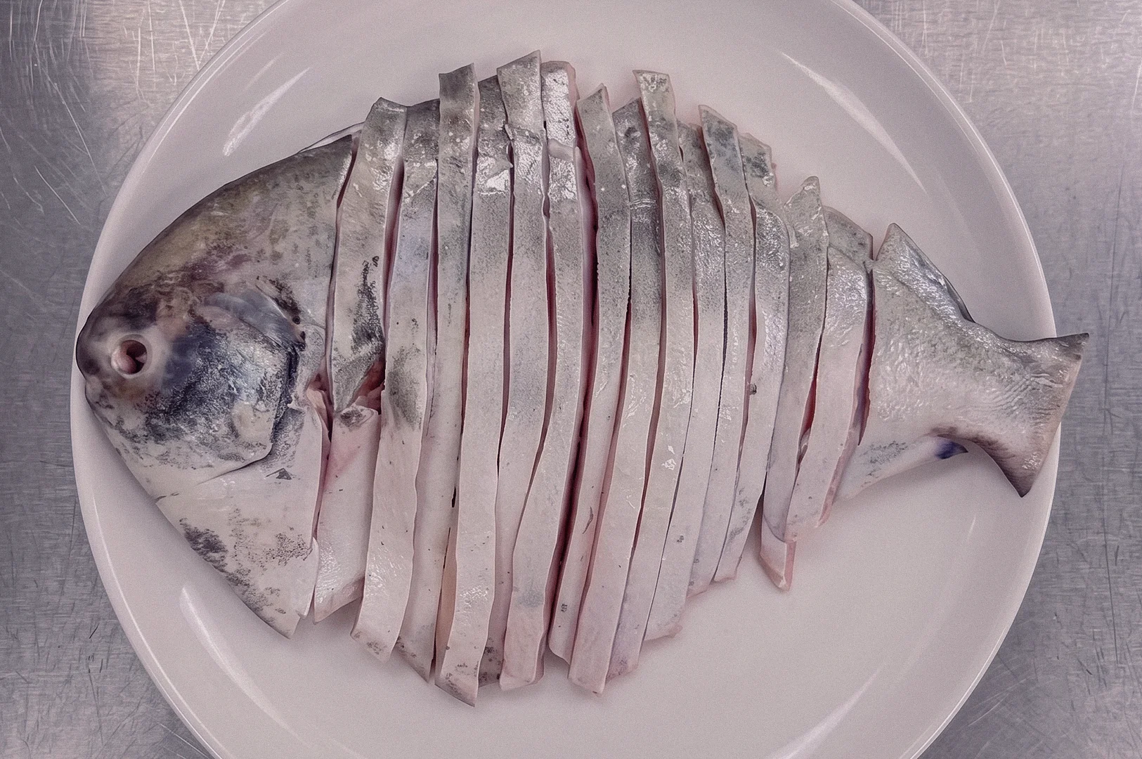 Overhead flat-lay shot of freshly sliced pomfret fish arranged on a white plate, showcasing the tender silver-skinned flesh used for traditional pomfret fish soup and clear collagen broth recipes in Singapore.