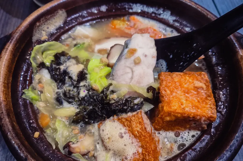 Steaming collagen-rich fish soup in Singapore with fresh fish slices, tofu, seaweed, cabbage and mushrooms in a traditional claypot, close-up angled food photography highlighting comforting local flavours.