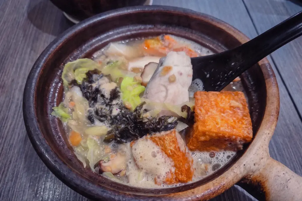 Close-up angled shot of pomfret fish soup in a claypot, showing flaky pomfret fish, fried tofu, shiitake mushrooms, cabbage, and seaweed in a savoury collagen-rich broth.