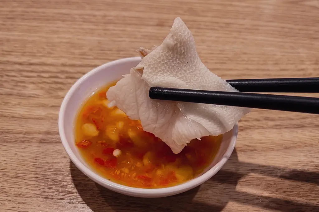 Tender white pomfret fish dipped into chilli sauce with chopsticks, showcasing the soft silky texture that makes white pomfret ideal for clear fish soup and premium seafood dishes.