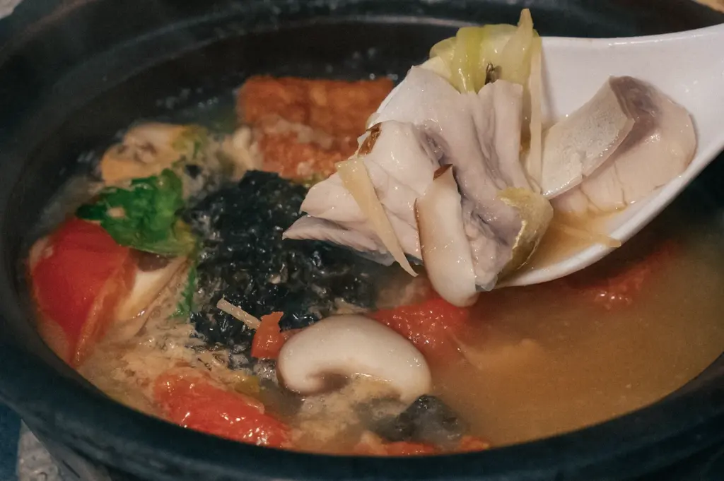Close-up side-angle view of sliced white pomfret served in a steaming seafood soup with mushrooms and vegetables, showcasing the fish's tender flesh and premium culinary appeal.