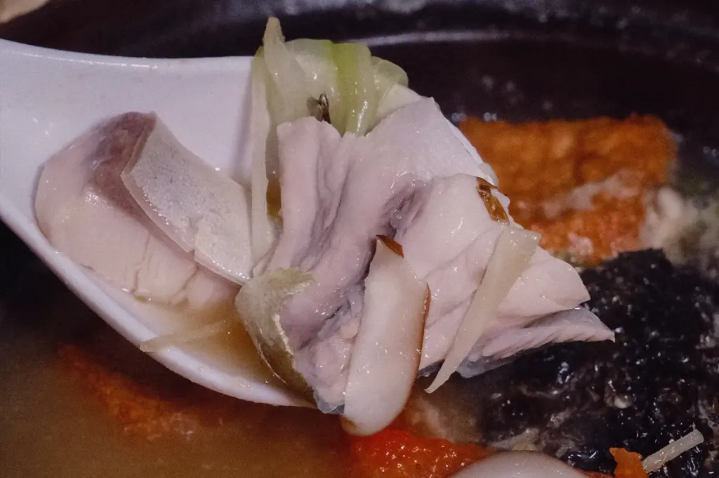 Macro close-up shot highlighting tender, perfectly timed pomfret fish slices and fresh ginger on a soup spoon held above a claypot.