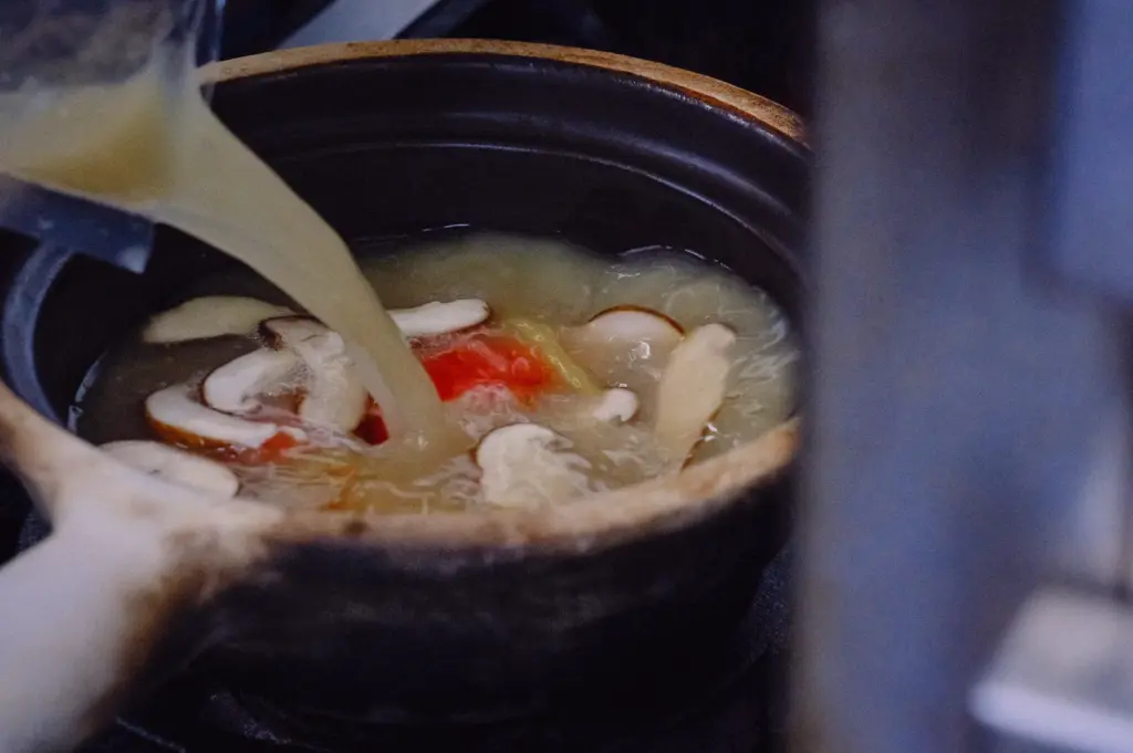 Fish bone broth being poured into a claypot fish soup with shiitake mushrooms, tomato and ginger, showcasing a naturally collagen-rich broth that creates the balanced flavour of traditional pomfret fish soup.