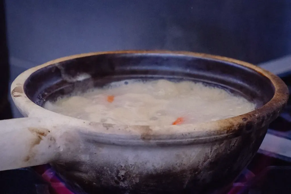 High-angle close-up of collagen-rich Singapore fish soup simmering in a traditional pot over an open flame, showcasing creamy fish bone broth preparation.
