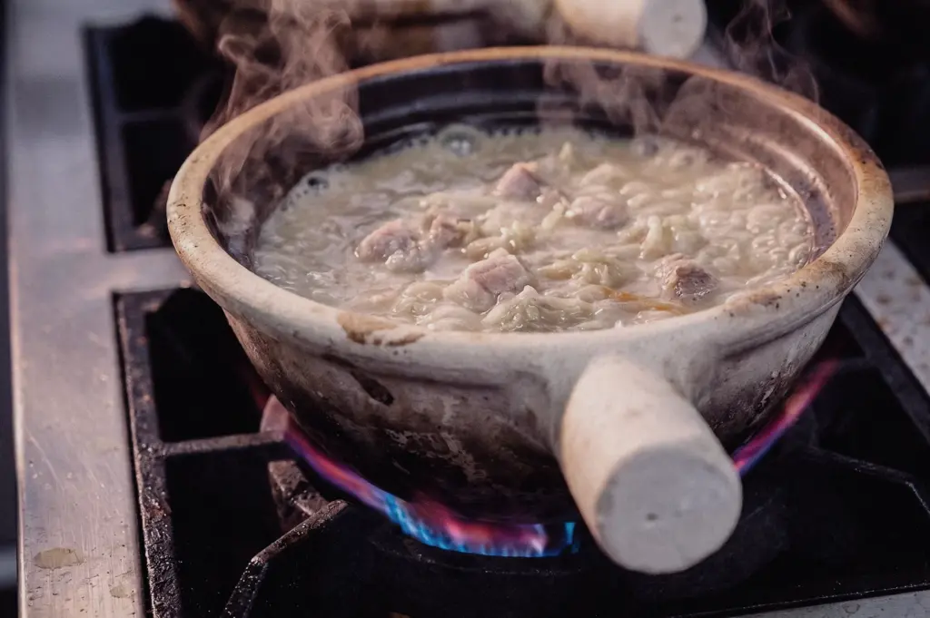 Low-angle close-up of claypot Pomfret Fish Soup simmering over an open flame, featuring tender fish, vegetables and naturally thick collagen broth in a traditional Singapore fish soup preparation.