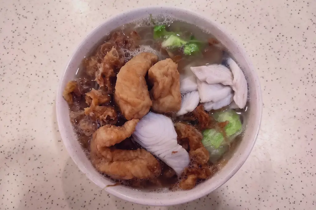 Overhead, top-down shot of a bowl of Singapore fried fish soup combining golden crispy fried fish nuggets and poached raw fish slices in a rich broth with vegetables.