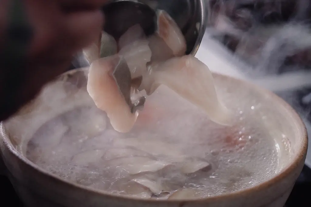 Extreme close-up, slightly high-angle view of tender pomfret fish slices being lifted from a steaming bowl of pomfret fish soup. The delicate white fish fillets and clear aromatic broth highlight the freshness, premium quality, and refined texture that make pomfret one of the most sought-after seafood delicacies in Asian cuisine.