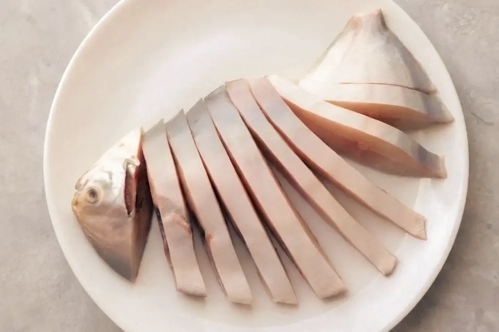 Overhead flat-lay view of freshly sliced white pomfret arranged on a white plate, emphasizing the fish's thick, boneless cuts and reputation as a premium seafood delicacy.