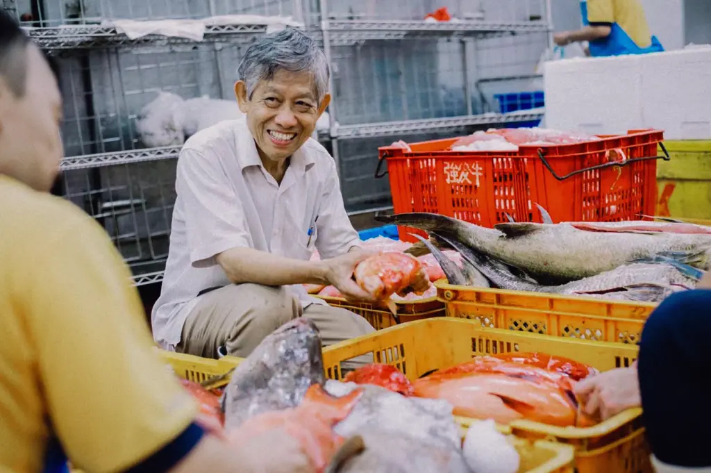 Fresh seafood supplier sorting premium fish at a Singapore seafood market, surrounded by crates of locally sourced fish, captured at eye-level angle to showcase the family trade behind Hup Lok's fresh fish soup.