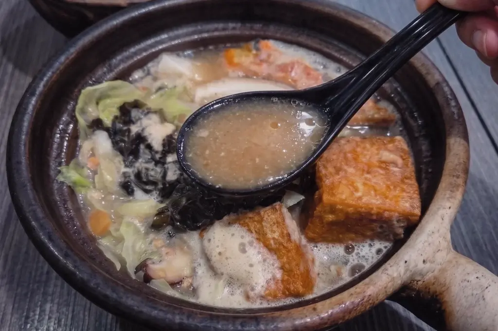 Close-up three-quarter angle of Grandpa's Pomfret Fish Soup in a traditional claypot, featuring collagen-rich fish broth, pomfret fish, tofu, cabbage and mushrooms with a spoonful of flavorful Singapore fish soup.