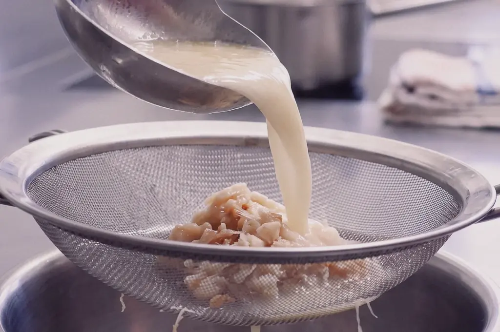 Close-up high-angle shot of collagen-rich fish broth being poured through a fine mesh strainer to make traditional Teochew fish soup, separating fish bones and ingredients for a clear, flavorful Singapore fish broth.