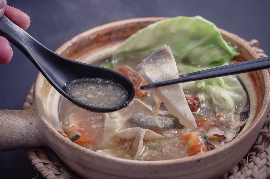 White pomfret fish lifted from a bowl of Grandpa's Pomfret Fish Soup with collagen-rich broth, vegetables, mushrooms and tomato, highlighting the fish's soft silky texture.