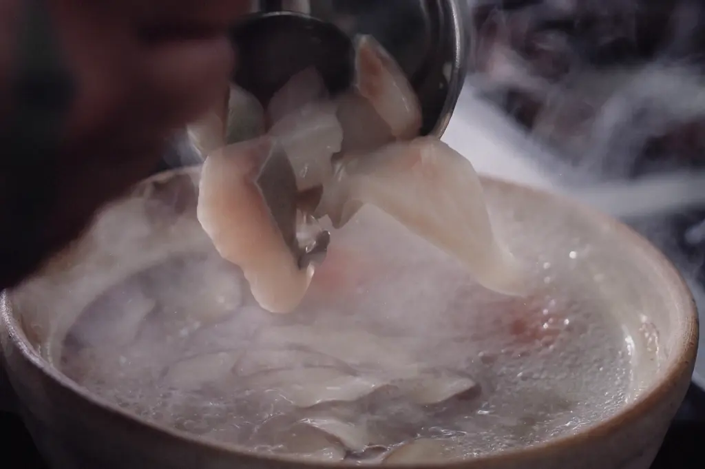Extreme close-up, slightly high-angle view of tender pomfret fish slices being lifted from a steaming bowl of pomfret fish soup. The delicate white fish fillets and clear aromatic broth highlight the freshness, premium quality, and refined texture that make pomfret one of the most sought-after seafood delicacies in Asian cuisine.