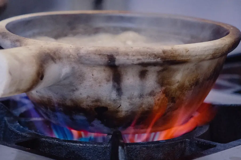 Low-angle eye-level shot focusing on a rustic, heat-stained claypot sitting directly over live stove flames.