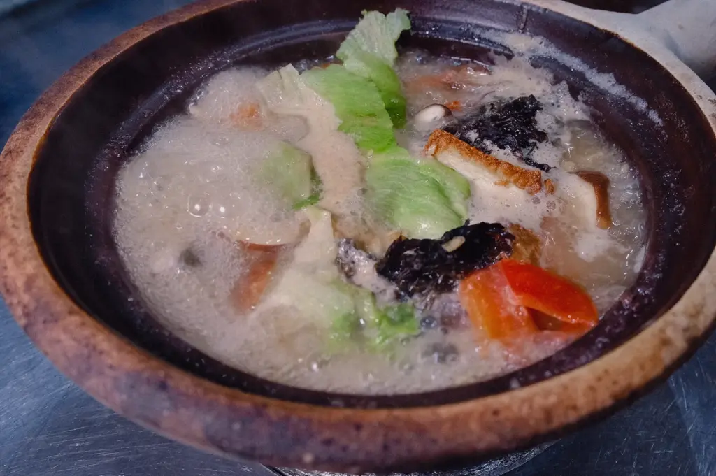 Top-down flat lay shot capturing a bubbling claypot filled with rich fish soup broth and green vegetables.