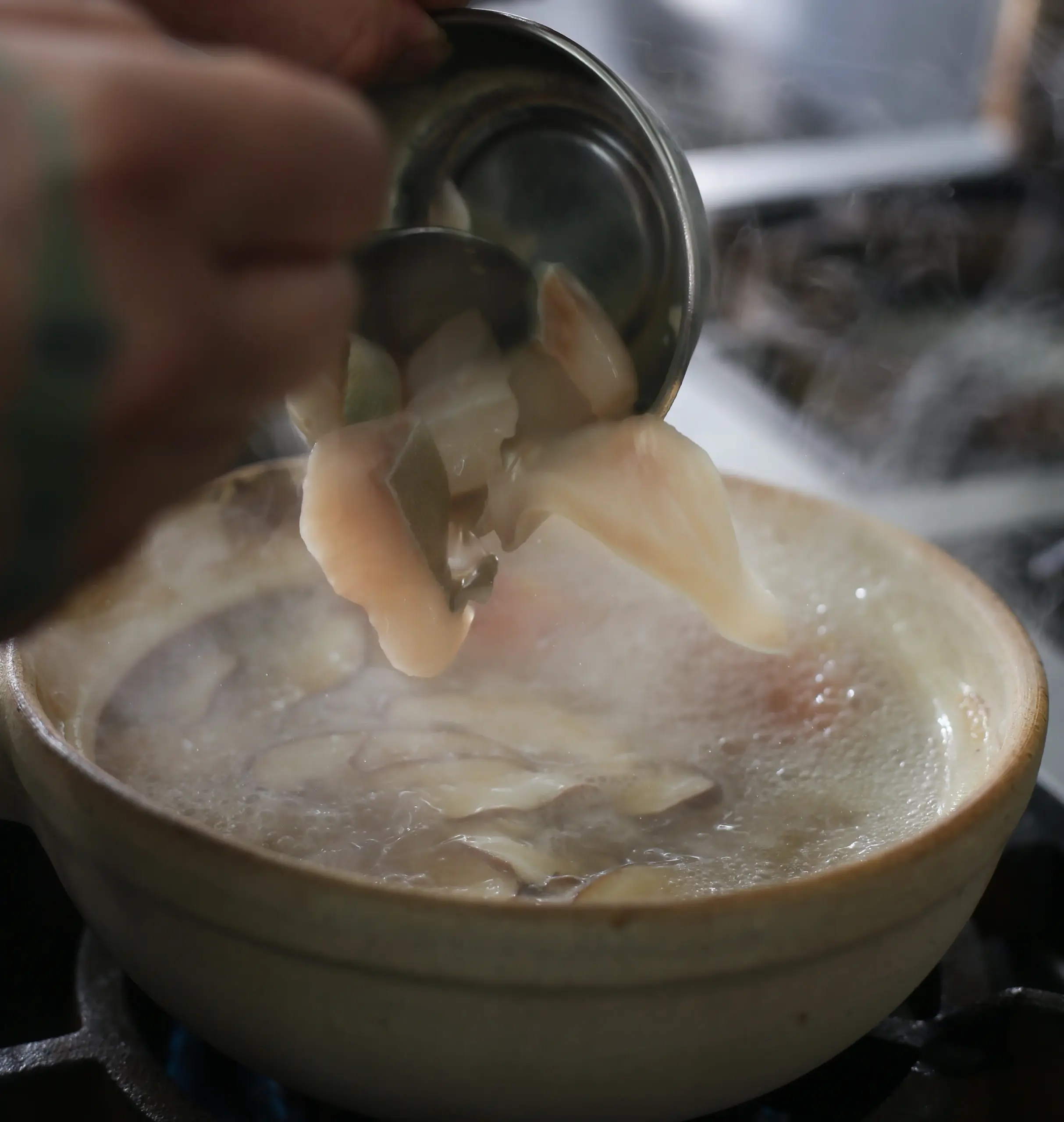 Extreme close-up, slightly high-angle view of tender pomfret fish slices being lifted from a steaming bowl of pomfret fish soup. The delicate white fish fillets and clear aromatic broth highlight the freshness, premium quality, and refined texture that make pomfret one of the most sought-after seafood delicacies in Asian cuisine.