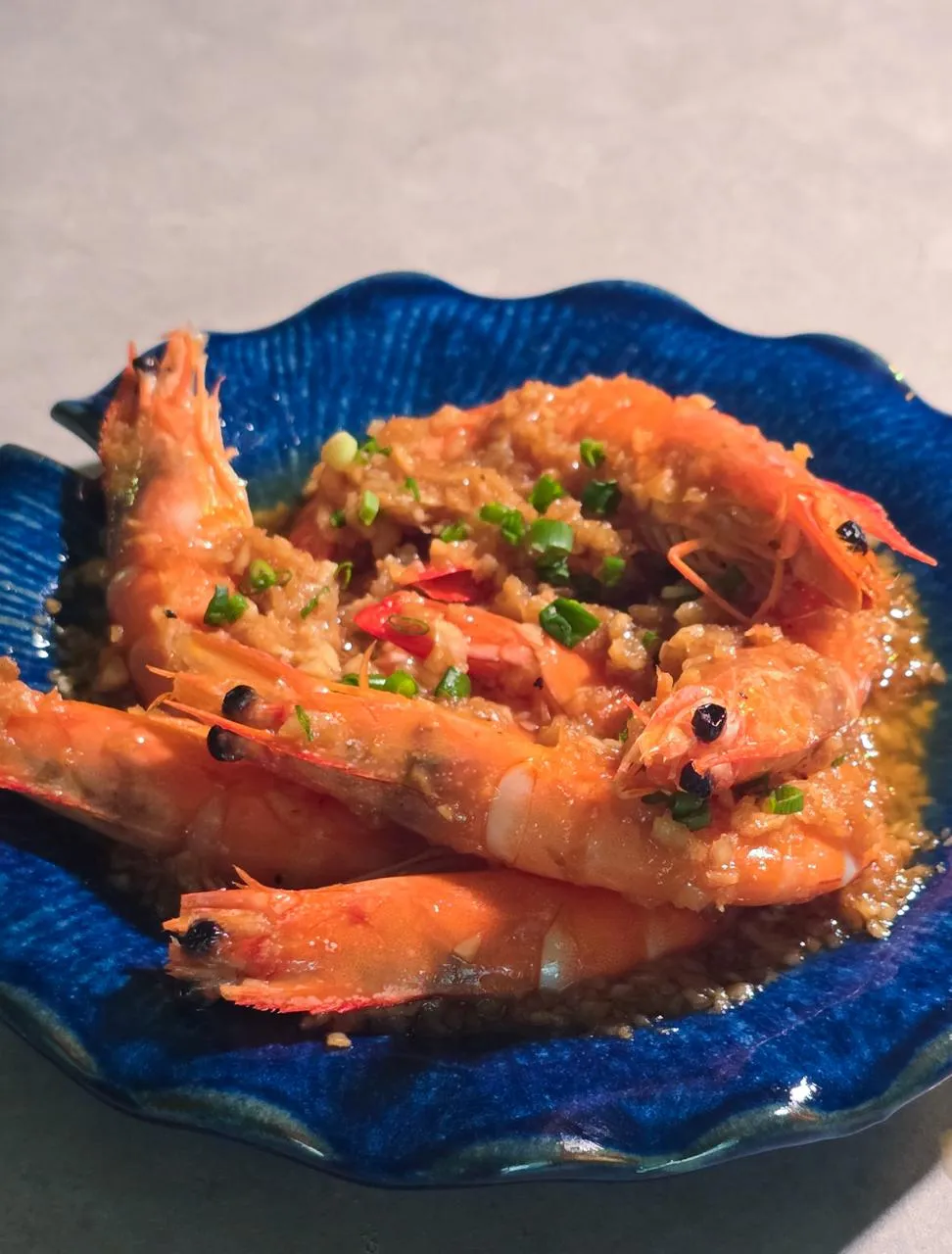 Close-up 45-degree angle shot of Garlic 'Kami no Ebi' Prawns (蒜蓉蒸神之海老), featuring premium whole prawns topped with minced garlic, scallions, and vermicelli noodles in a flavorful steamed seafood sauce, served on a blue ceramic platter.