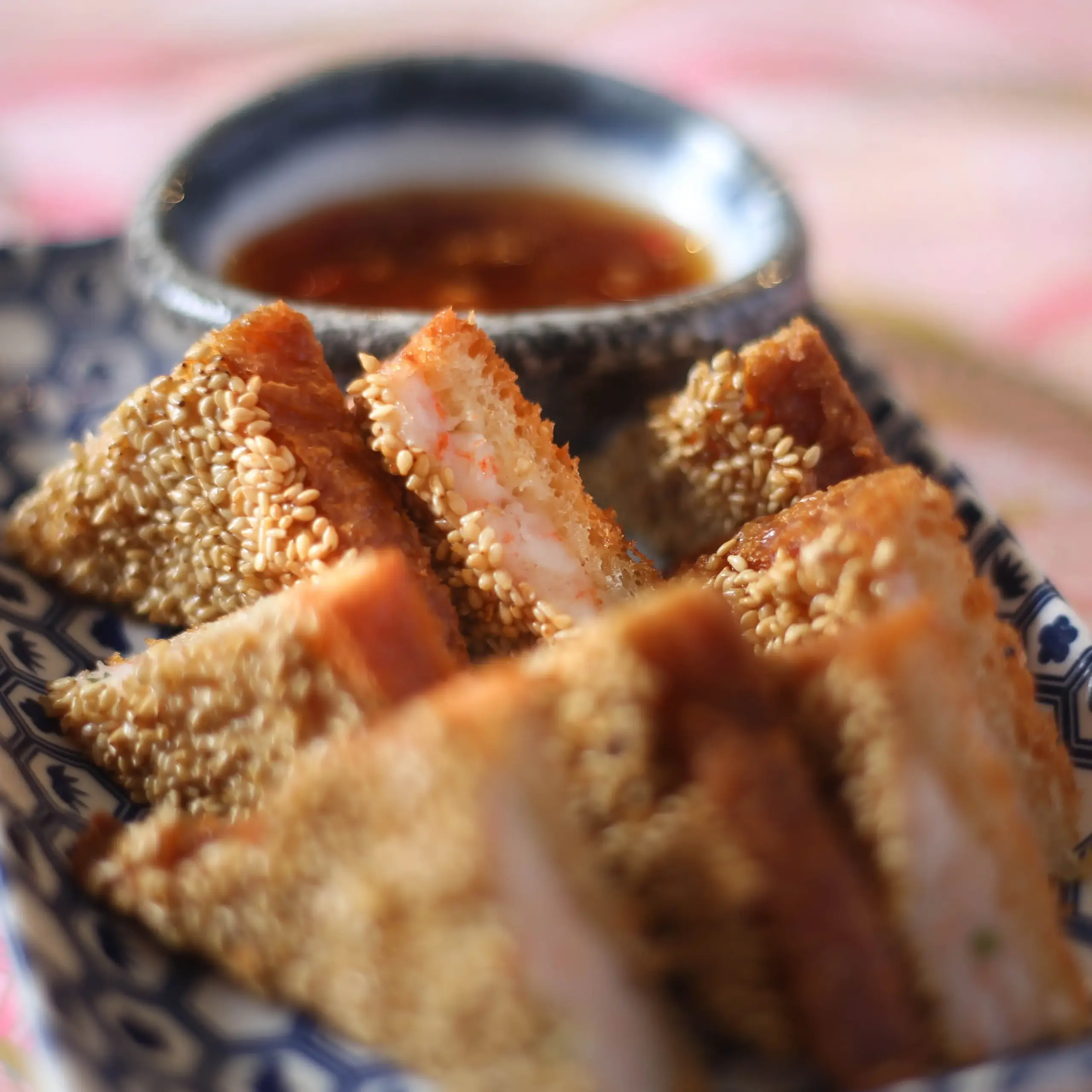 Close‑up angled shot of several triangular pieces of Asian‑inspired fried rice or shrimp toast arranged on a dark rectangular plate, each with a crunchy golden breaded crust, soft white filling, and sprinkled sesame seeds, emphasizing the contrast of textures and colors in this Japanese or fusion appetizer dish.