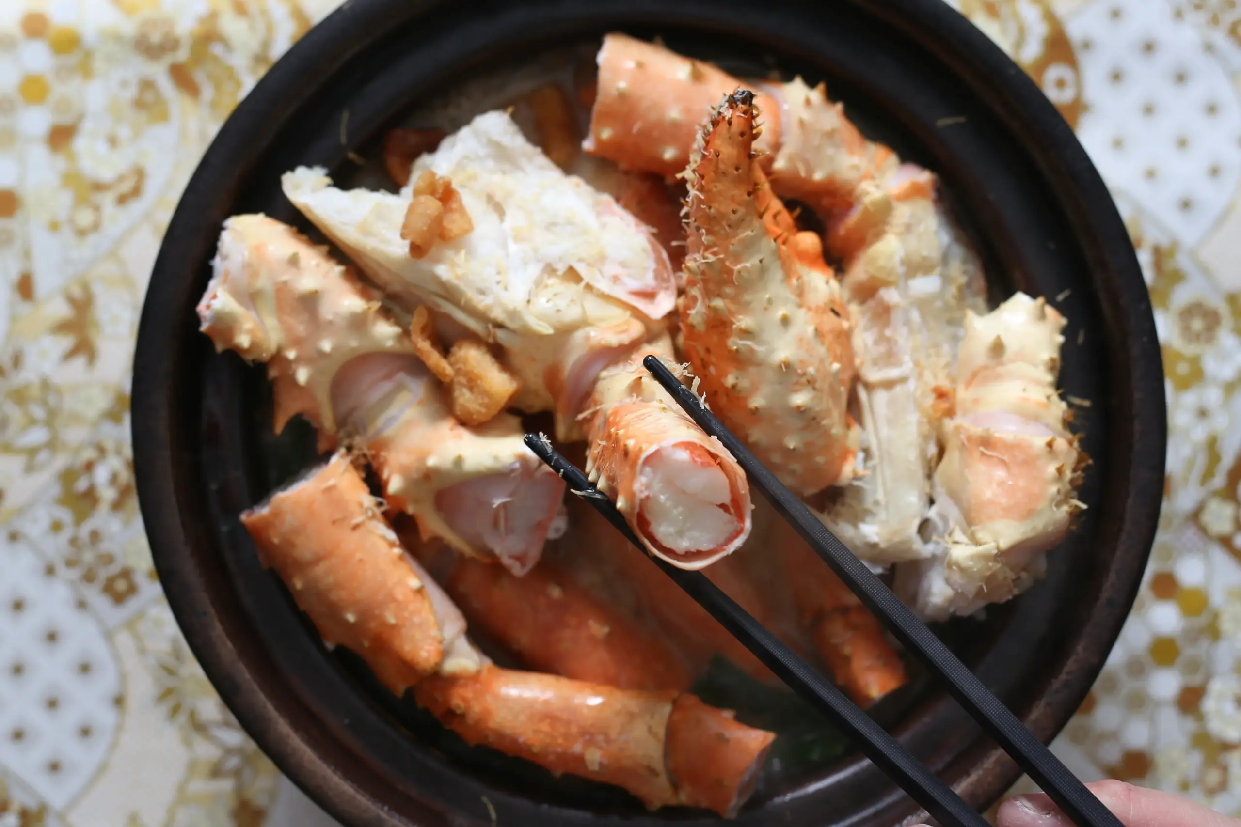 Overhead close-up shot of premium king crab bee hoon served in a rustic clay pot, featuring succulent king crab leg meat held with chopsticks above delicate rice vermicelli noodles for a luxurious seafood dining experience.