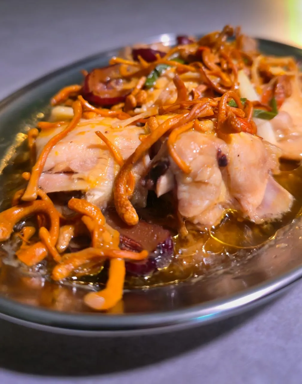 Close-up 45-degree overhead angle shot of Steamed Chicken with Cordycep Mushrooms (虫草花蒸鸡), featuring tender chicken pieces, cordycep flowers, scallions, and rich steamed broth served in a ceramic dish.
