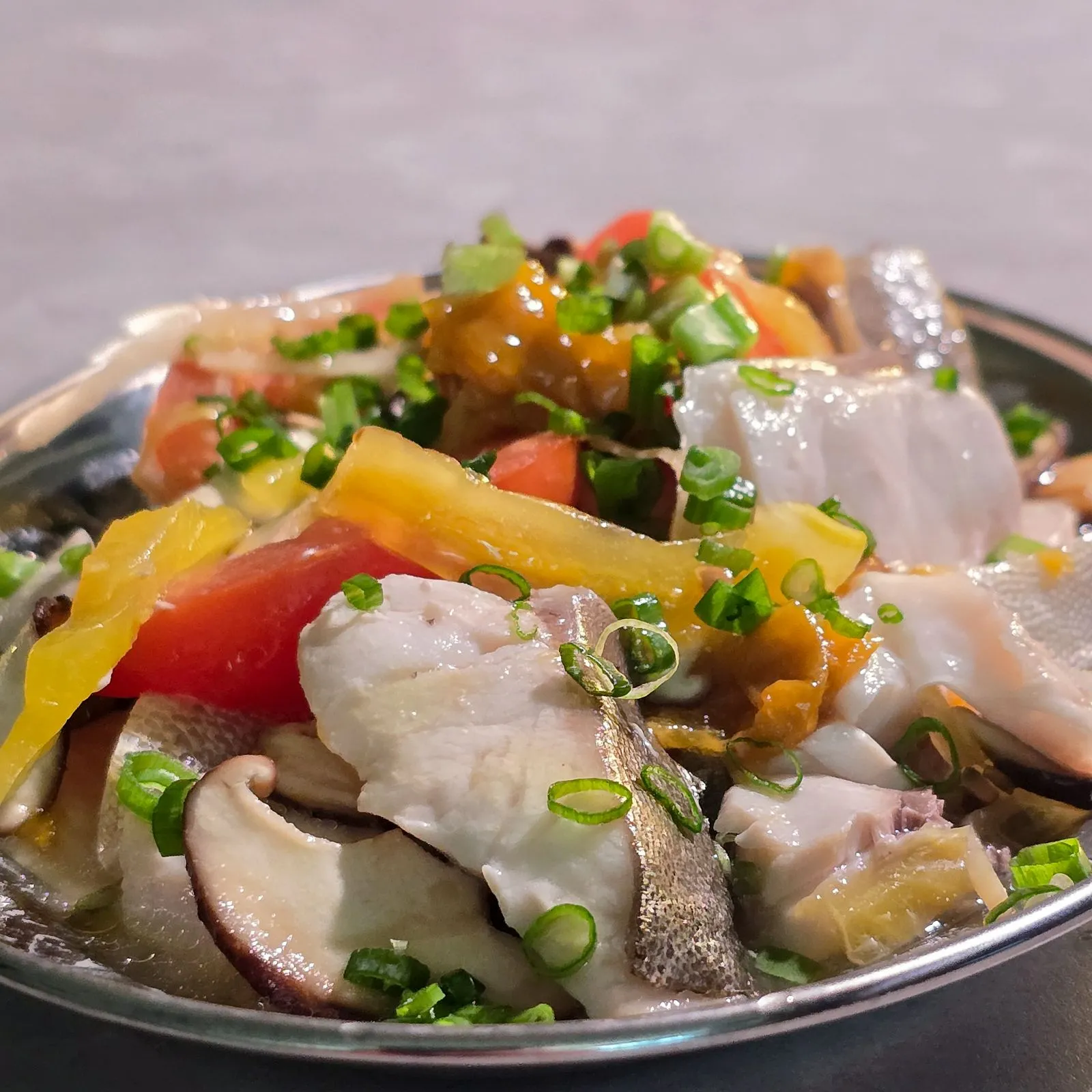 Close-up 45-degree angle shot of Teochew Steamed Pomfret (Boneless), featuring tender white pomfret fish, sliced bell peppers, scallions, and savory Teochew-style sauce, served in a shallow metal dish at a Chinese restaurant.