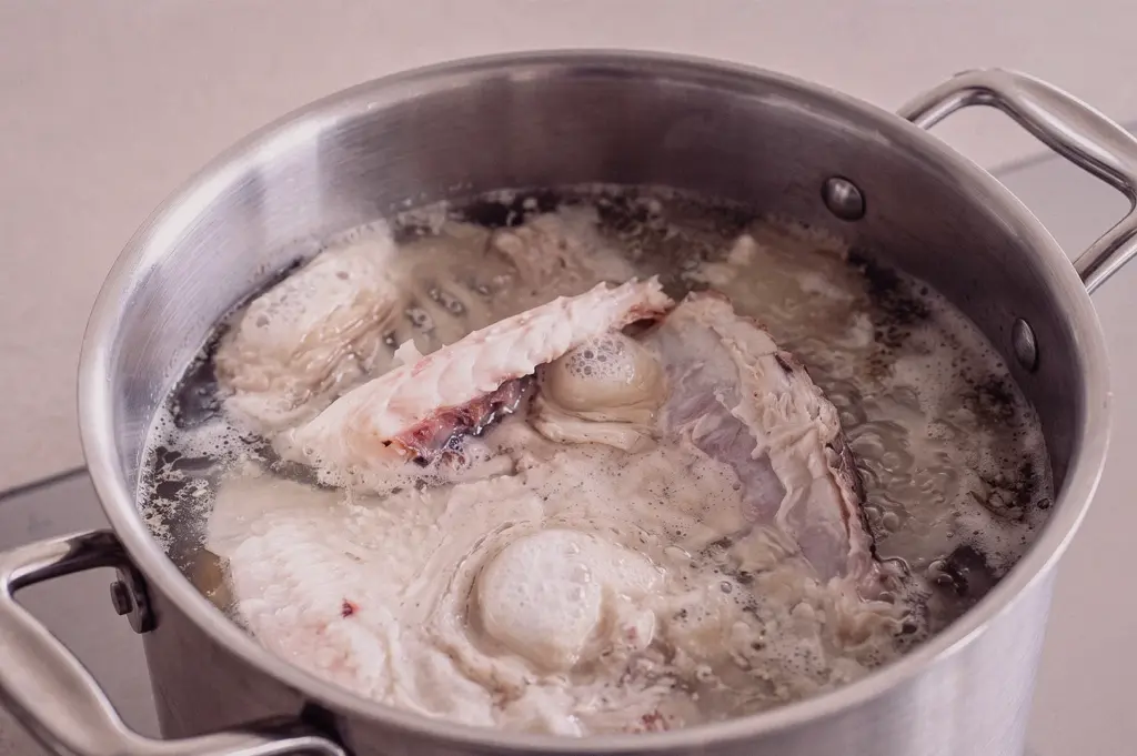 A top-down overhead flat lay shot captures fish bones and trimmings simmering inside a large stainless steel stockpot to extract collagen for stock