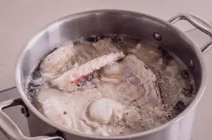 A top-down overhead flat lay shot captures fish bones and trimmings simmering inside a large stainless steel stockpot to extract collagen for stock