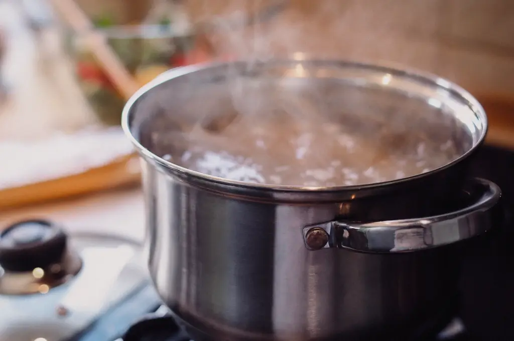 A side-angle close-up shot shows steam rising from a stainless steel stockpot of fish soup broth simmering steadily on a stove top.