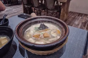 High-angle close-up shot showcasing a claypot of steaming pomfret fish soup with tofu puff, mushrooms, and seaweed resting on a woven mat at Hup Lok.