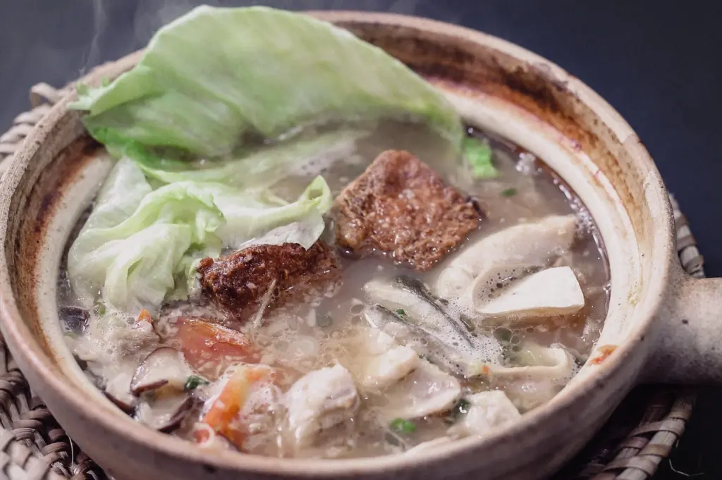 A high-angle close-up shot highlights tender pomfret fish slices, leafy greens, and fried tofu simmered in a steaming claypot of collagen fish broth.