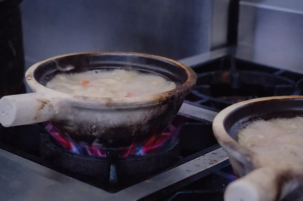 Low-angle close-up shot of claypots simmering on gas stove burners filled with rich ivory fish broth made from batang bones and tee poh.