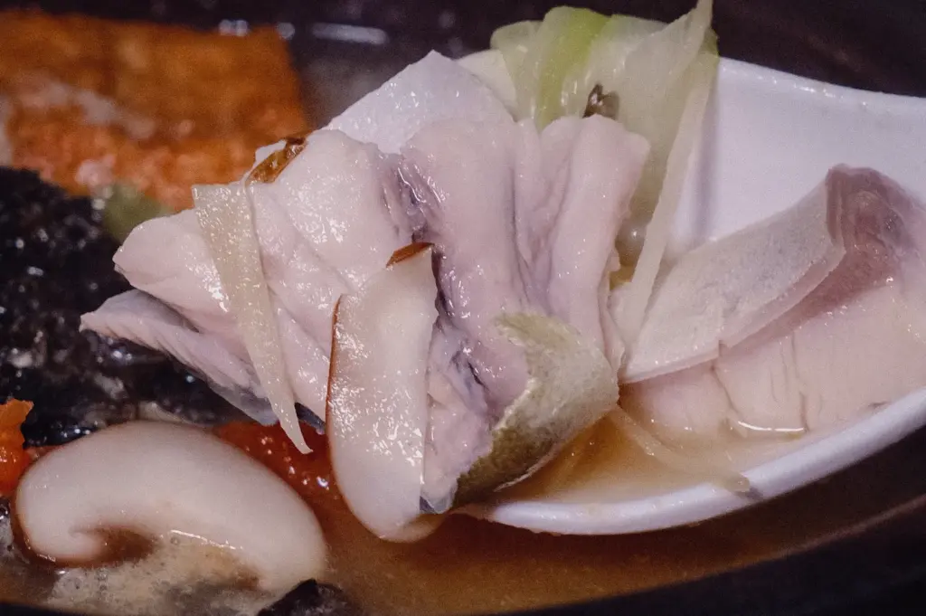 An extreme close-up shot captures a spoon lifting delicate, tender pomfret fish slices topped with fine ginger strips out of a rich collagen soup.