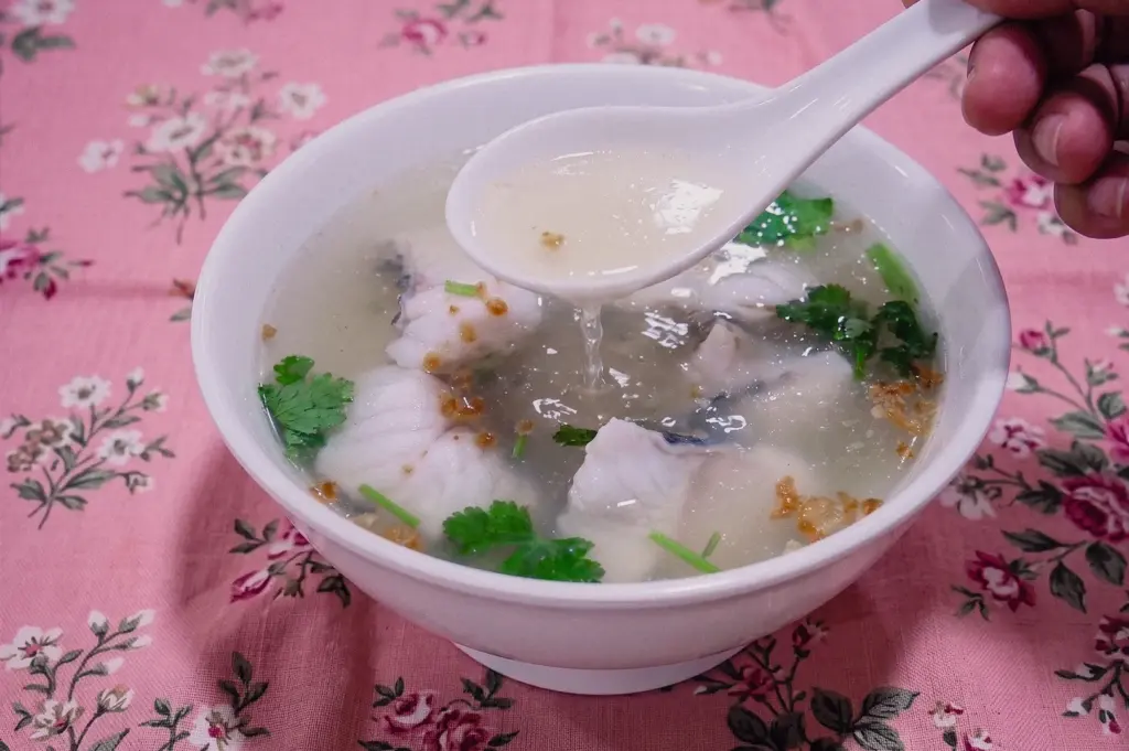 Close-up shot capturing a white ceramic spoon scooping broth from a bowl of clear Teochew fish soup to showcase its transparency and lightness.