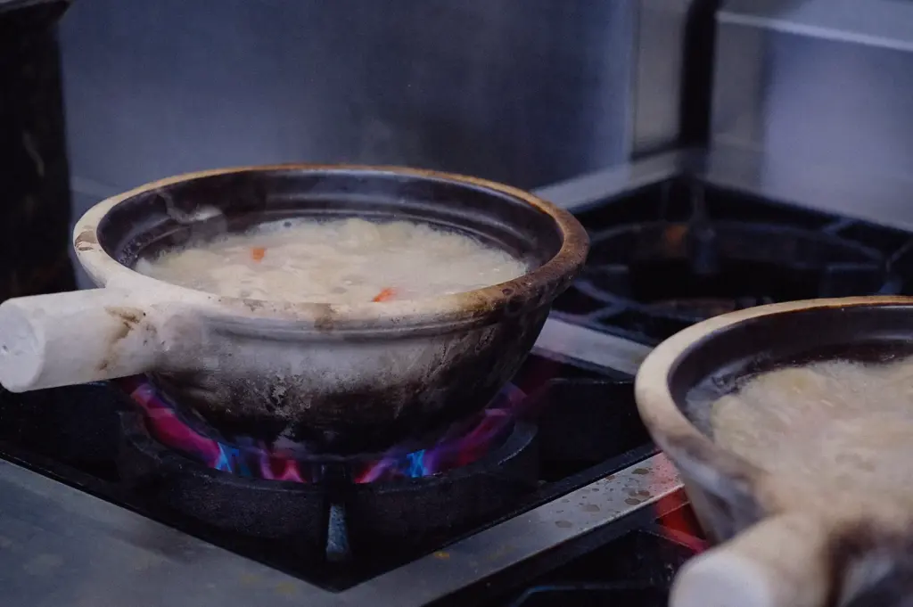 A close-up side-angle shot shows collagen fish broth maintaining a gentle, controlled simmer inside a claypot over a gas burner.