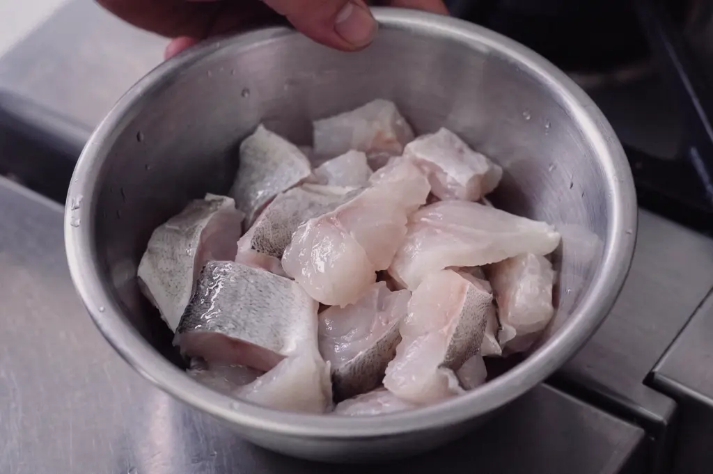 High-angle close-up shot displaying a stainless steel bowl filled with fresh, raw pomfret fish slices ready for cooking.