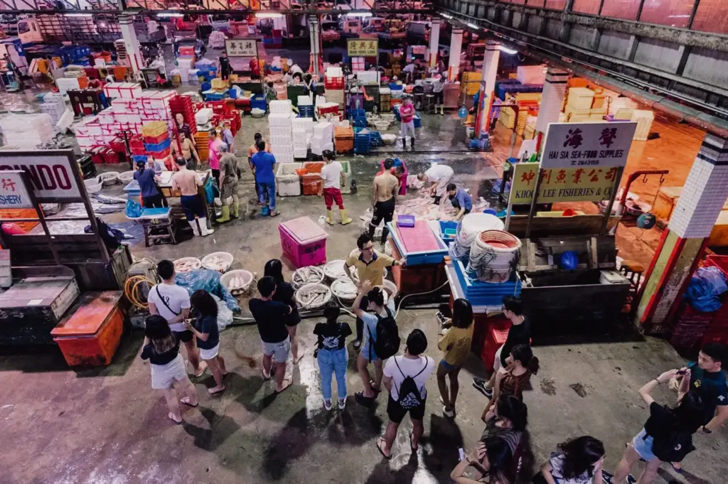 High-angle wide shot overlooking the lively Hai Sia Seafood market floor at Jurong Fishery Port with buyers and fishmongers gathered around seafood stalls.