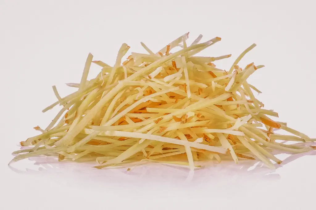 A straight-on eye-level macro shot captures a neat mound of freshly julienned ginger strips isolated against a clean white background.