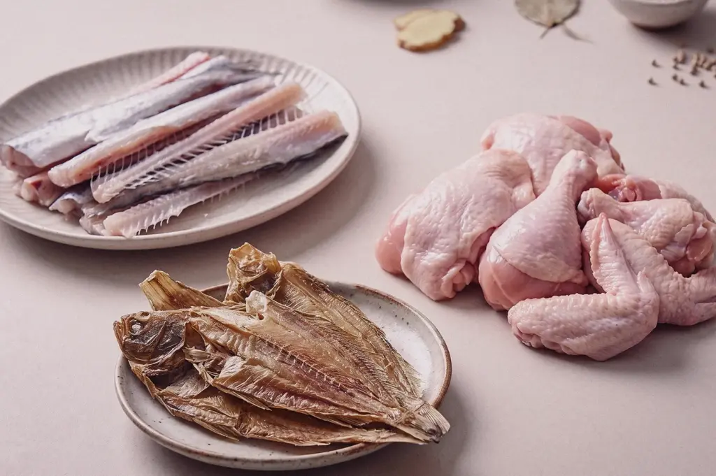 A top-down overhead flat lay shot displays the core raw broth ingredients, including fresh batang fish bones, raw chicken drumsticks, and dried sole fillets (tee poh).