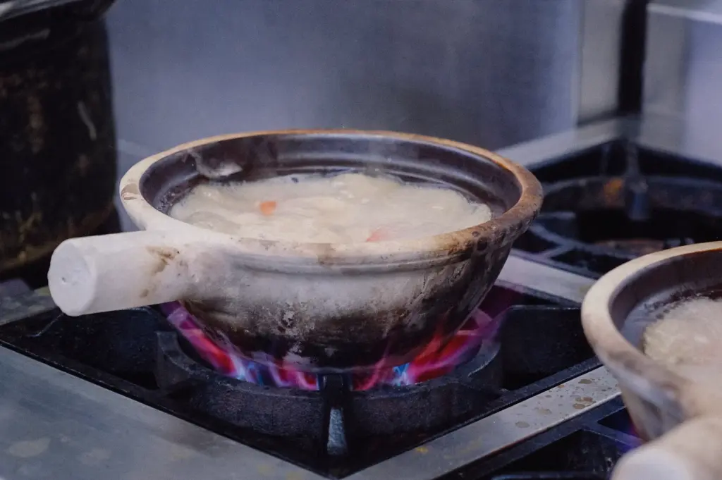 A side-angle close-up shot highlights a claypot of collagen fish broth boiling rapidly over high gas stove flames.