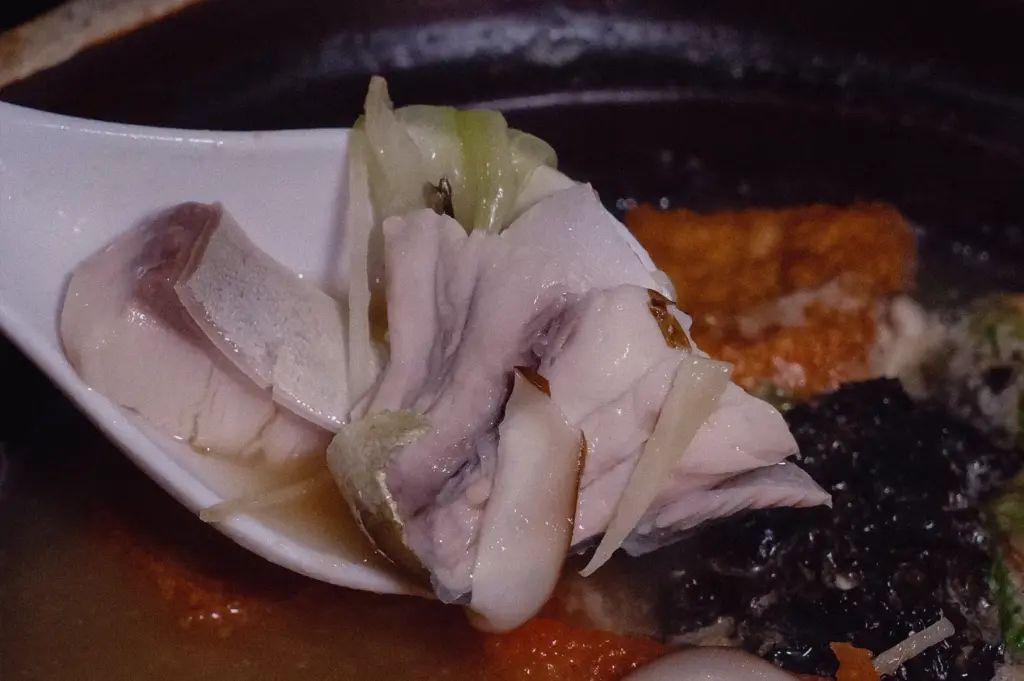 An extreme close-up action shot features a soup spoon lifting delicate, silky pomfret fish slices topped with julienned ginger out of a rich fish broth.