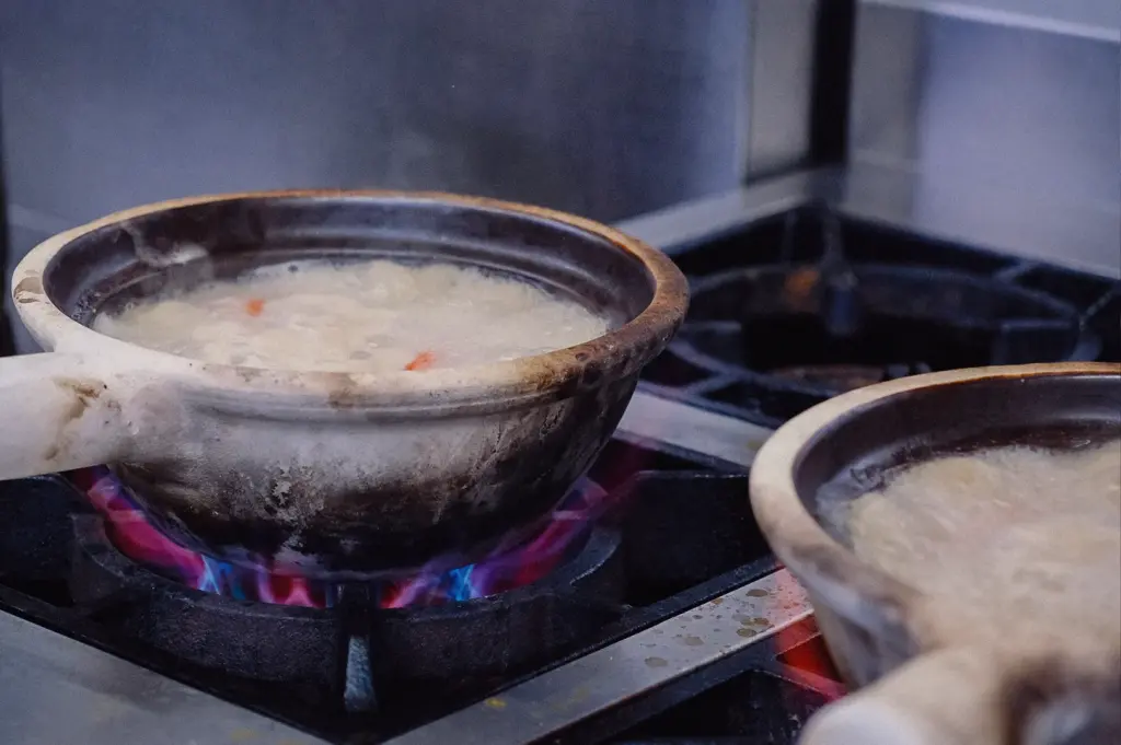 A side-angle close-up shot displays collagen fish soup simmering inside a claypot over high gas flames on a commercial stove.