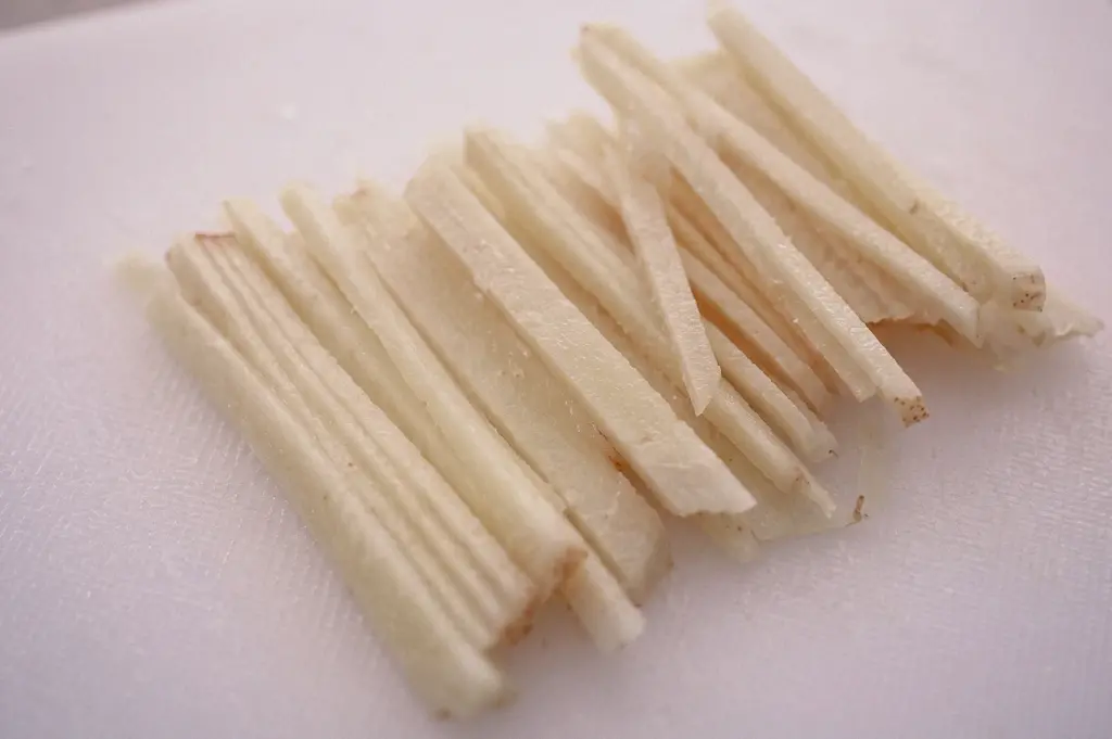 High-angle close-up shot detailing neatly julienned fresh ginger matchsticks arranged on a white cutting board.