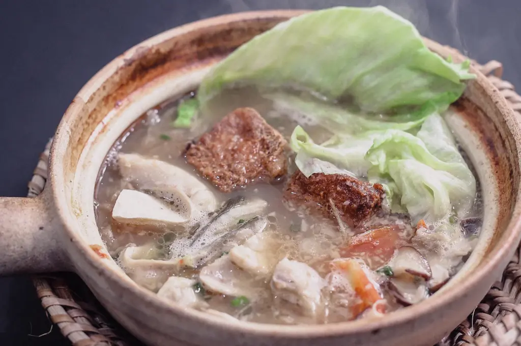 An overhead high-angle shot reveals a hot claypot overflowing with tender pomfret fish slices, cabbage, tomatoes, and rich fish broth.